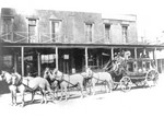 The Modox stagecoach with six people on top, that ran from Tombstone to Bisbee. Buildings appear to be Tombstone.