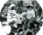 A Papago family, which appears to be a mom with two small children, surrounded by ollas in Bisbee.