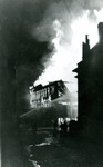 The Phelps Dodge Company store on fire in 1938. Firemen are attempting to put the fire out. Spectators are watching. The store was built in 1904.