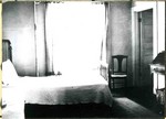 A bedroom inside the Young Women's Christian Association, YWCA, showing a bed, secretary, large window, and a chair. The YWCA was located on Howell Avenue in Bisbee.