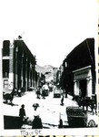 A view of Bisbee's Main Street. The Bank of Bisbee and the Copper Queen Library can be seen. A carriage, horses, wagons, and people milling on the street are visible. The photo has Library and PO written in the appropriate locations.