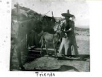 An unidentified woman in a sombrero with an adult and baby burro. Bottom of photo reads: Friends. An ocotillo fence or corral can be seen in the background.