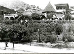 An exterior view of the original Young Women's Christian Association, YWCA, with the YMCA in the background. There are some people in the yard and the walls are covered with vegetation.