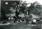 The chuck wagon of the Frank Proctor Ranch in the San Rafael Valley, Arizona. It is captioned, The Mess, and shows a group of men sitting around the wagon eating. Archie Smith is on the far right.