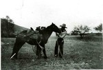 Two cowboys saddling a horse. It is captioned, Saddling a Bronchos.