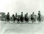 Six unidentified cowboys on horses. They are in front of a corral. They are: Fred Horne, George Parker, Duke Parker, Lee Parker, Jim Sutherland, and Willie Parker.