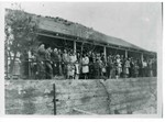 Photograph of a crowd of people attending a wedding, standing atop the wall along OK Street. The house in the background is probably Leo Medigovich's. The small child front left is Betty Bugen.