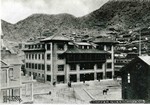 Photograph postcard showing the Copper Queen Hotel and the hills behind it, circa 1904. The Bisbee Daily Review is to the right of the hotel. The Copper Queen Consolidated Mining Company General Office Building is in front of the hotel, and the white Bessemer House is to the far left side of the photo. Photo captioned: Copper Queen Hotel. Photo by Humphries Photo Company and published in El Paso, Texas.