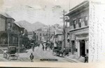 Photograph postcard showing Main Street, circa 1904. Horses and buggies are parked along the side of the street and a line of men are marching down the middle. The Bank of Bisbee is on one corner and the old library is on the other. Photo simply captioned: Main Street. Photo by Humphries Photo Company and published in El Paso, Texas.