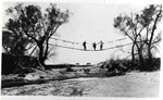 Photograph of three men on a swinging bridge over the San Pedro River. The bridge was accessed at either end by ladders.