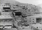 Photograph looking north up the hill from upper Main Street, 1915. The Palace Livery is on the right in the foreground, and the Masonic Lodge is on the left. There is a banner on the bottom of the Masonic Lodge that reads: --- CK Reducing sale, ---mter sale of house furnishings good, ---got the cash YOUR CREDIT IS GOOD. There are a number of buggies parked between the two buildings.